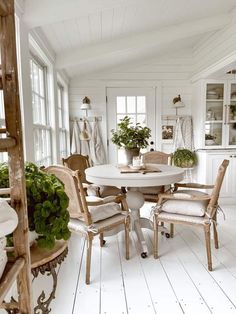 a white table and chairs in a room with wood flooring, potted plants and windows