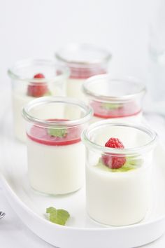 four desserts in small glass containers on a white platter with raspberries