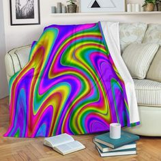 a colorful blanket sitting on top of a wooden floor next to a white couch and book