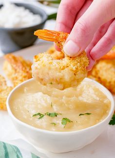 a person dipping shrimp into a bowl of dip with bread croutons in the background