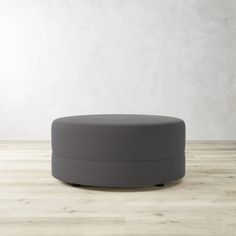 a grey round ottoman sitting on top of a wooden floor next to a white wall