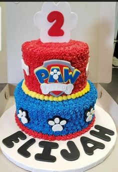 a two tiered cake with paw patrol decorations on the top, and paw's first birthday sign