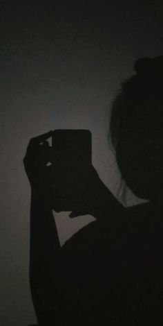 the silhouette of a woman taking a photo with her cell phone in the dark room