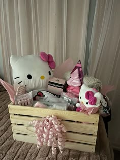 a hello kitty stuffed animal sits in a wooden crate on a bed with pink bows