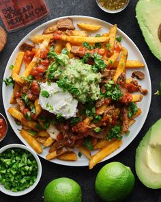 a white plate topped with french fries covered in guacamole and sauce next to sliced avocado