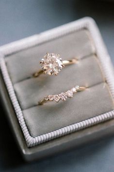 two engagement rings sitting on top of a velvet ring box, with one diamond in the middle