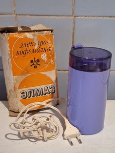 a purple cup sitting on top of a counter next to a box and charger