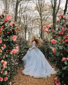 a woman in a blue dress is walking through some bushes and flowers with her hair blowing in the wind