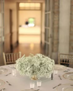 the table is set with white linens and gold place settings, along with baby's breath flowers