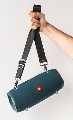 a person holding a bluetooth speaker in their hand with the strap down to it