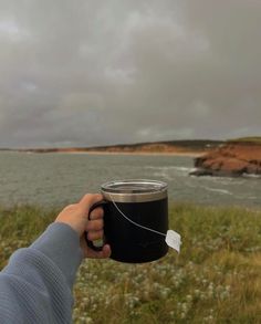 a person holding a coffee cup in front of a body of water on a cloudy day