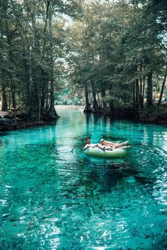 two people are floating on a raft in the middle of a river with blue water