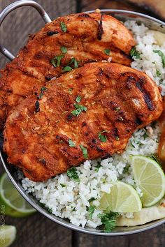 two pieces of chicken on top of rice and limes