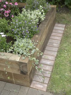 a wooden planter filled with lots of flowers on top of a brick walkway next to grass