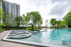 an outdoor swimming pool surrounded by greenery and trees with buildings in the back ground