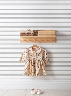 a baby's shirt hanging on a wall next to a pair of shoes and a coat rack