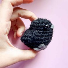 a hand holding a small crocheted black and white animal brooch on a pink background