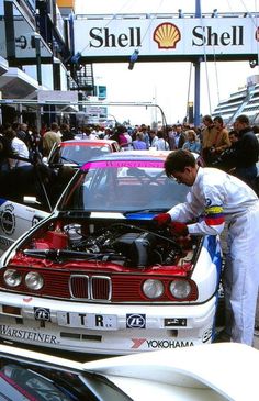 a man working on the hood of a car in front of other cars and people