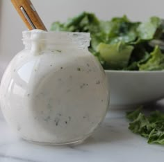 a salad in a jar next to a bowl of lettuce and a wooden spoon