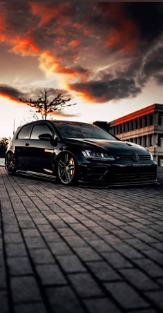 a black car parked on the side of a brick road next to a tall building