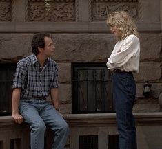 a man and woman are sitting on a ledge looking into each other's eyes