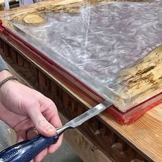 a person holding a pair of scissors in front of a piece of wood that has been stained red