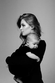 a woman holding a baby in her arms while posing for a black and white photo