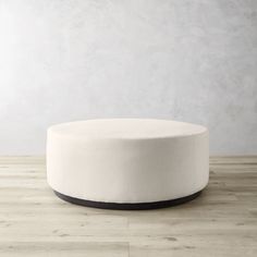 a white round ottoman sitting on top of a hard wood floor next to a wall