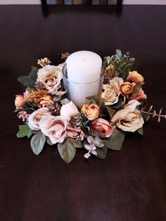 a white candle sitting on top of a wooden table next to some flowers and leaves