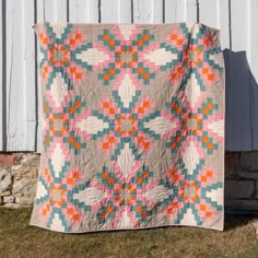 a quilt is hanging on the side of a white building with grass in front of it