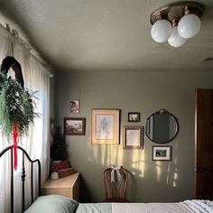 a bed sitting in a bedroom next to a window with white curtains and pictures on the wall