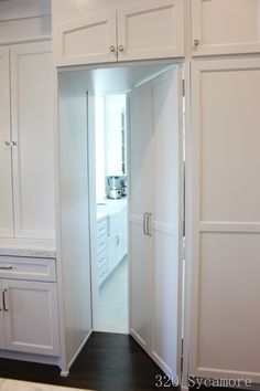 an open door leading into a kitchen with white cupboards and drawers on either side