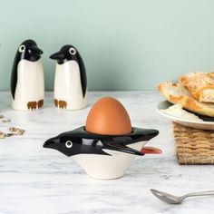 an egg holder with two penguins on it next to some bread and other food items