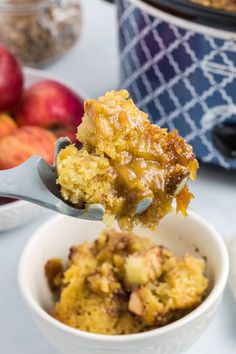 a close up of a spoonful of food in a bowl with apples behind it