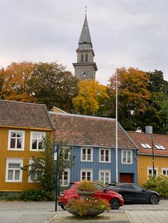 two cars are parked in front of colorful houses with a clock tower on the top