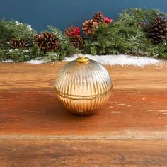 a gold vase sitting on top of a wooden table next to pine cones and evergreen branches