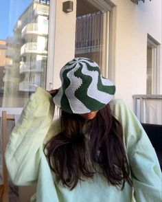 a woman wearing a green and white knitted hat looking out the window with her hands behind her head