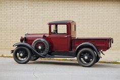 an old red truck is parked in front of a brick building with a tan wall