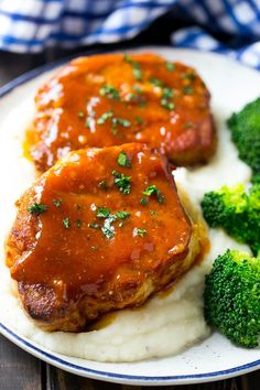 two pieces of meat covered in gravy on top of mashed potatoes and broccoli