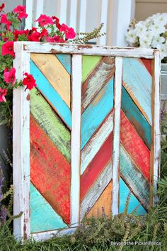 an old wooden box is decorated with colorful wood planks and flowers in the background