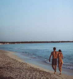 two people are walking on the beach near the water