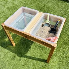 a wooden table with two bins filled with sand and shovels on the grass