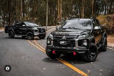 two black suvs driving down the road next to each other in front of trees