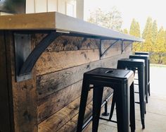 three stools are sitting at the bar in front of an outdoor kitchen with wood paneling