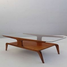 a glass and wood coffee table with two shelves on each side, in front of a white wall