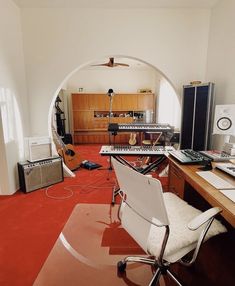 a room with a desk, chair and other musical equipment on it in front of a mirror