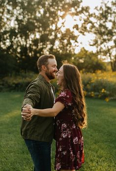 a man and woman are standing in the grass with their arms around each other as they laugh