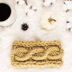 a knitted headband sitting on top of a white fur rug next to a cup of coffee