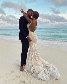 a man and woman standing on top of a sandy beach next to the ocean with their arms around each other