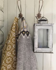 two knitted bags hanging from hooks on a white wall next to an old lantern